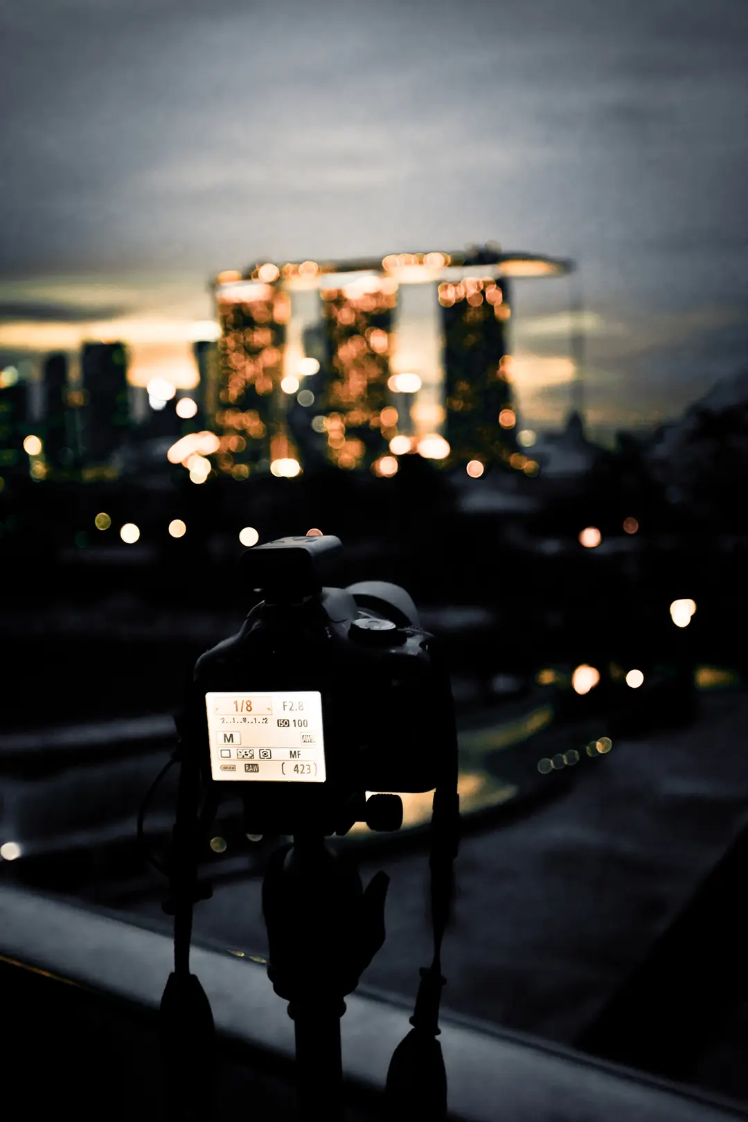 A camera on a tripod faces the Marina Bay Sands towers at dusk.