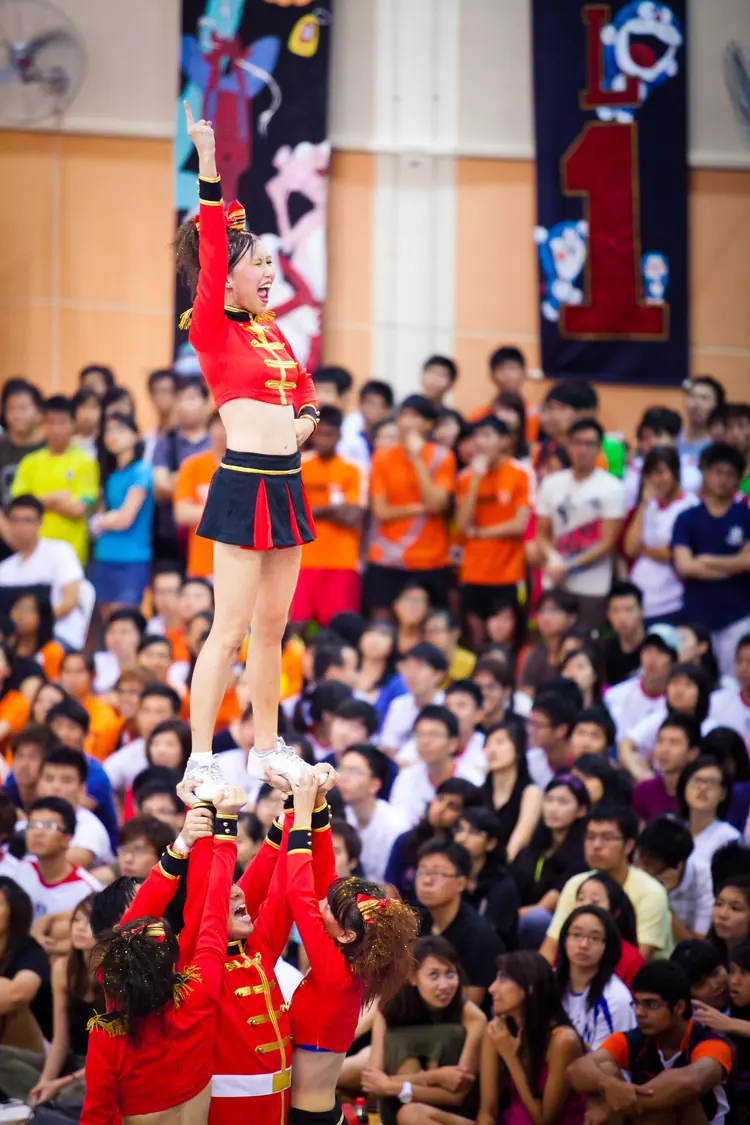 A cheerleader is lifted high above a packed crowd in a hall.