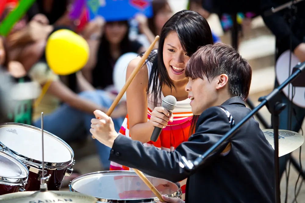 A singer leans in to a drummer during a live show.