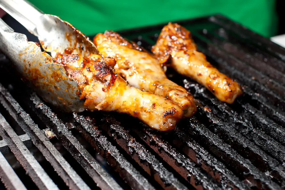 Chicken wings on a grill, turned with tongs.